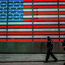 Two police officer men walking in front of an electronic USA flag in Time Square, New York, US