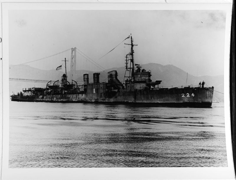 A black and white photo showing USS Stewart in the water with the Golden Gate bridge in the background. The water is calm and the vessel had two crew members standing on its bow. 