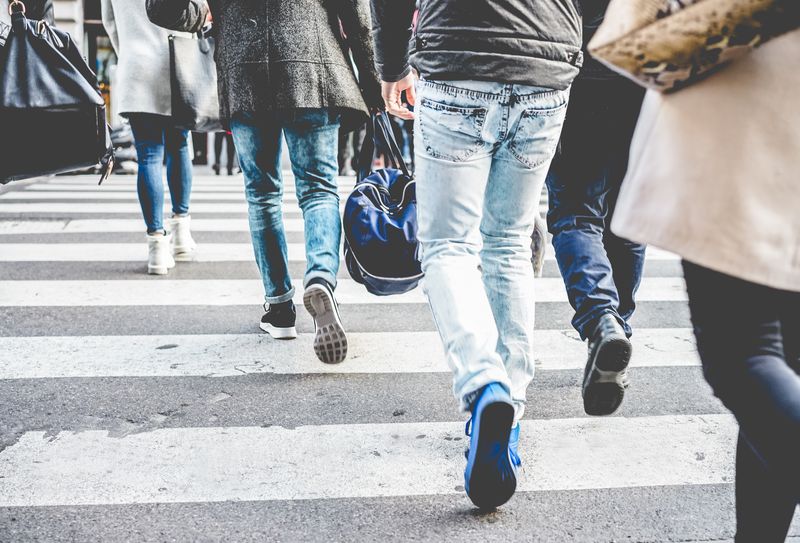 group of people walking away from the camera on a zebra crossing, pictured from the feet up to the waist