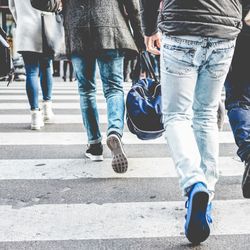 group of people walking away from the camera on a zebra crossing, pictured from the feet up to the waist