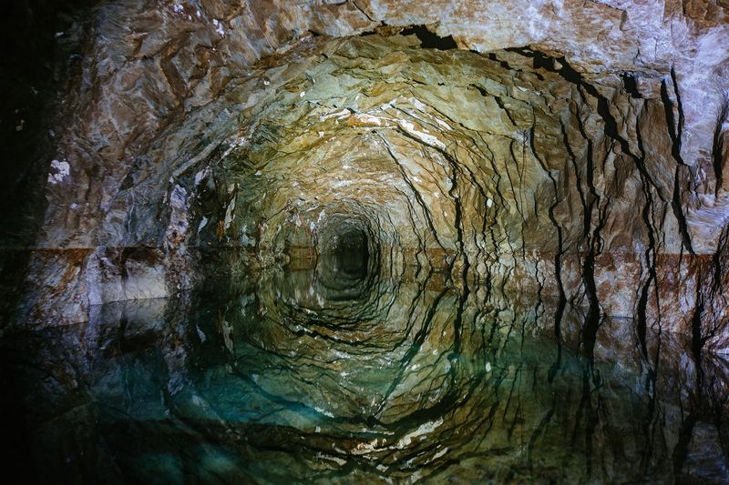 Dark flooded abandoned mine tunnel with water reflections.