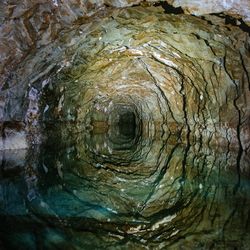 Dark flooded abandoned mine tunnel with water reflections.