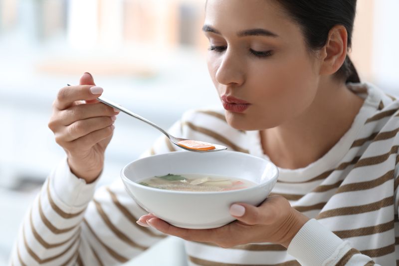 Woman blowing on a spoonful of vegetable soup