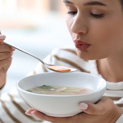 Woman blowing on a spoonful of vegetable soup