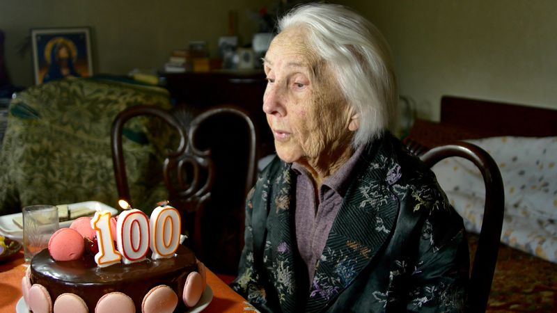 elderly woman sitting at table with a birthday cake, with candles in the shape of the number 100