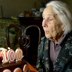 elderly woman sitting at table with a birthday cake, with candles in the shape of the number 100