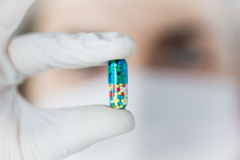 White gloved hand holds multi-coloured pill