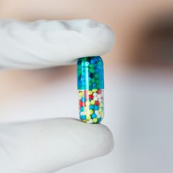 White gloved hand holds multi-coloured pill