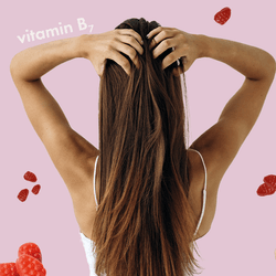 collage of images on a light pink background; there are pink, raspberry-shaped gummy vitamins, pill bottles, a hand showing the nails, a woman shown with her back to the viewer running her hands through her long brown hair, and illustrations of the chemical structure of biotin in white with the words "biotin" and "vitamin B7"