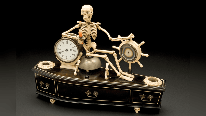 an old alarm clock of a skeleton sitting on a coffin