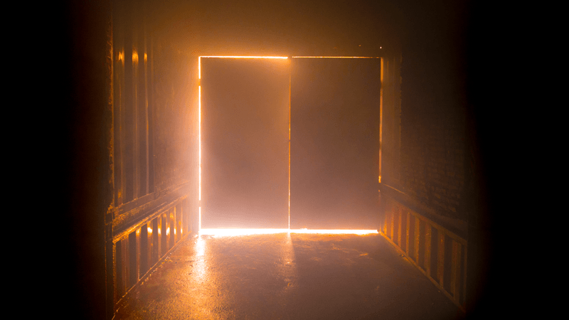 a dark corridor, the door at the end is backlit by a fire