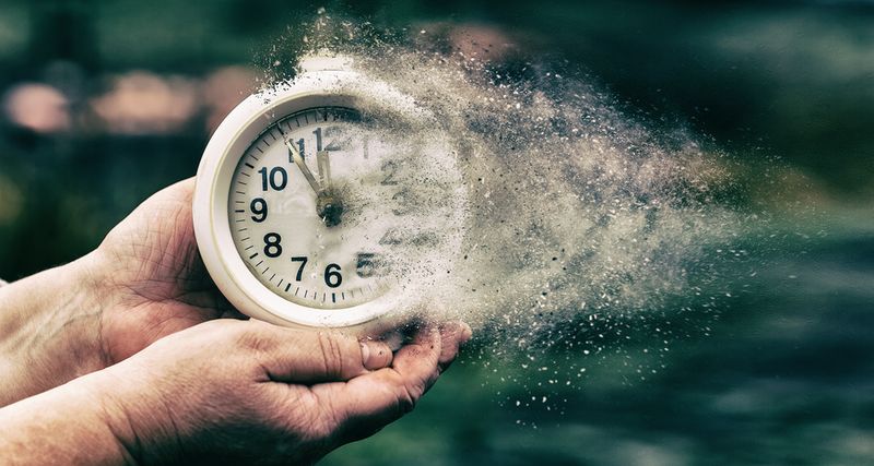 Person holding a white clock in both hands, the clock is dissolving into dust and blowing away to the right