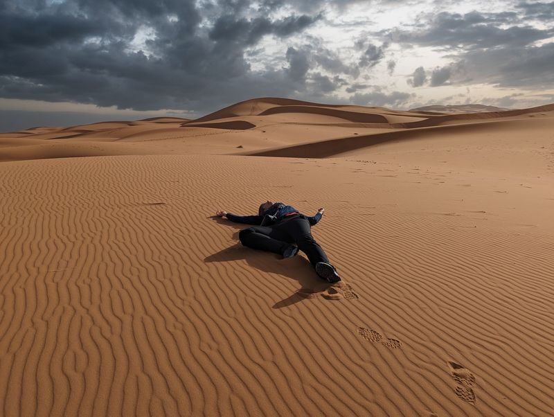 Photograph of person sprawled on their back in a sandy desert