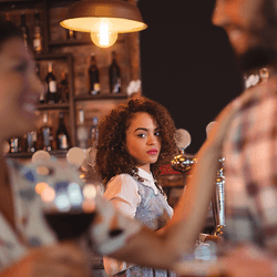 Two people flirting at a bar, a woman in the background looking jealous.