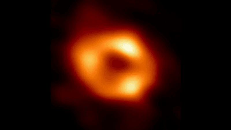 The event horizon telescope image of our galaxy's supermassive black hole, Sagittarius A*. An orange donut with some brighter spots is seen around a dark center where the black hole is