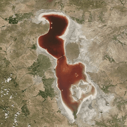 Two images of Lake Urmia. The first shows the lake under ideal conditions, with blue water; the second shows the lake on July 18, 2016, with vividly red water.