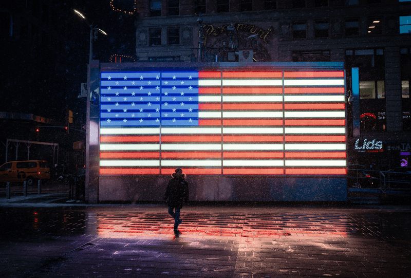 The silhouette of a person stands in front of an illuminated American flag in Times Square, New York City, during a snowstorm.