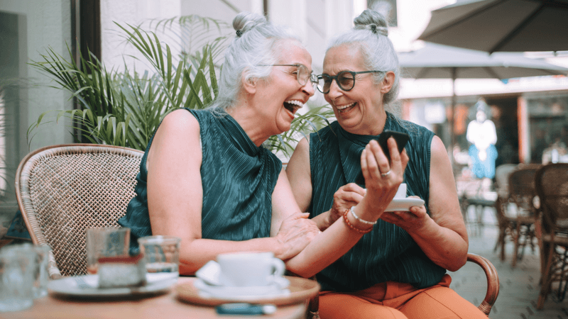 two older twins laughing together while having coffee in a cafe