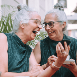 two older twins laughing together while having coffee in a cafe