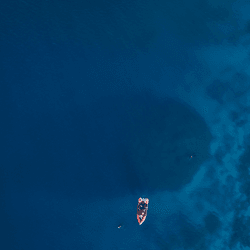 a tiny boat over the shadow of a massive coral